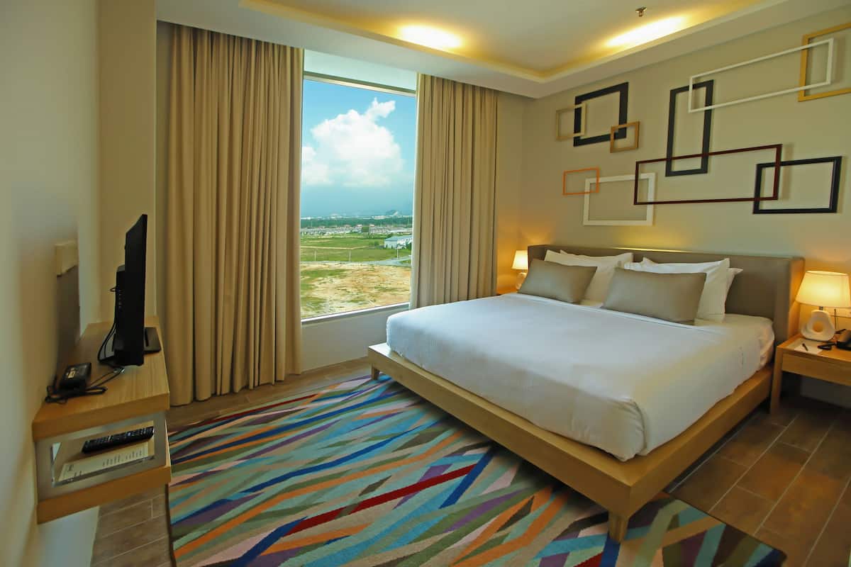 Habitación de hotel con una cama grande, televisión, escritorio con computadora y vista a la ciudad.