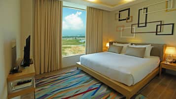 A hotel room with a large bed, a TV, a desk with a computer, and a view of the city.