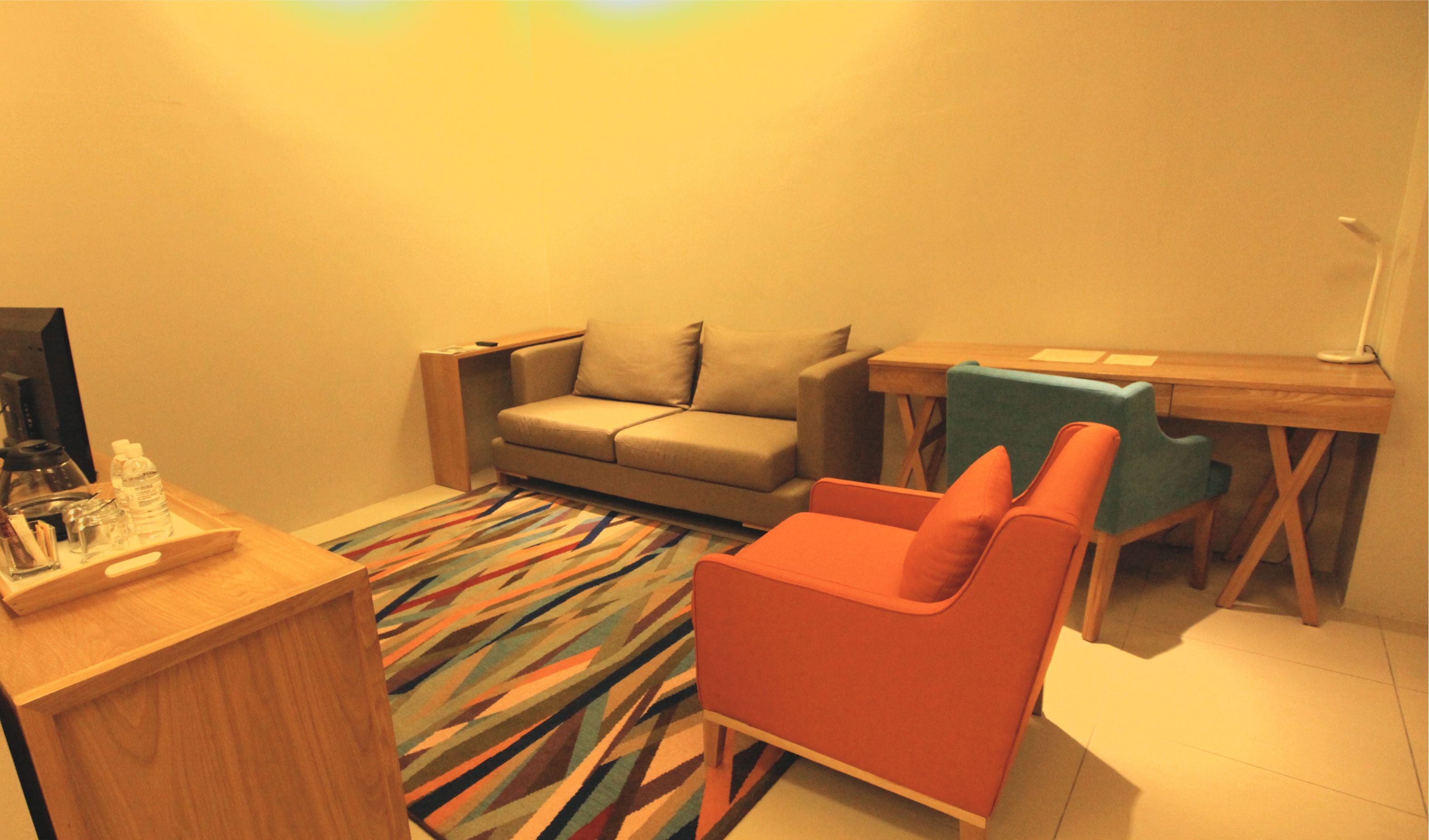 A compact living space with a sofa, a small desk, a chair, and a coffee machine.