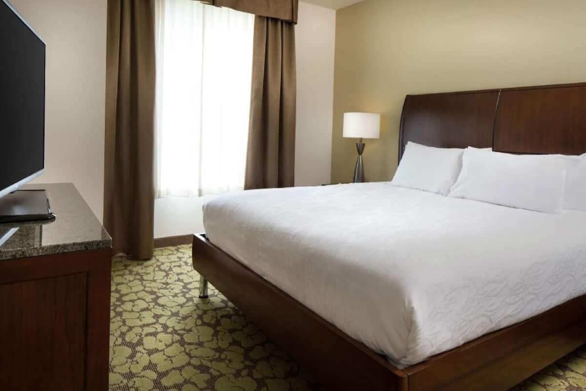 A hotel room with a bed, a desk, a lamp, and a television.