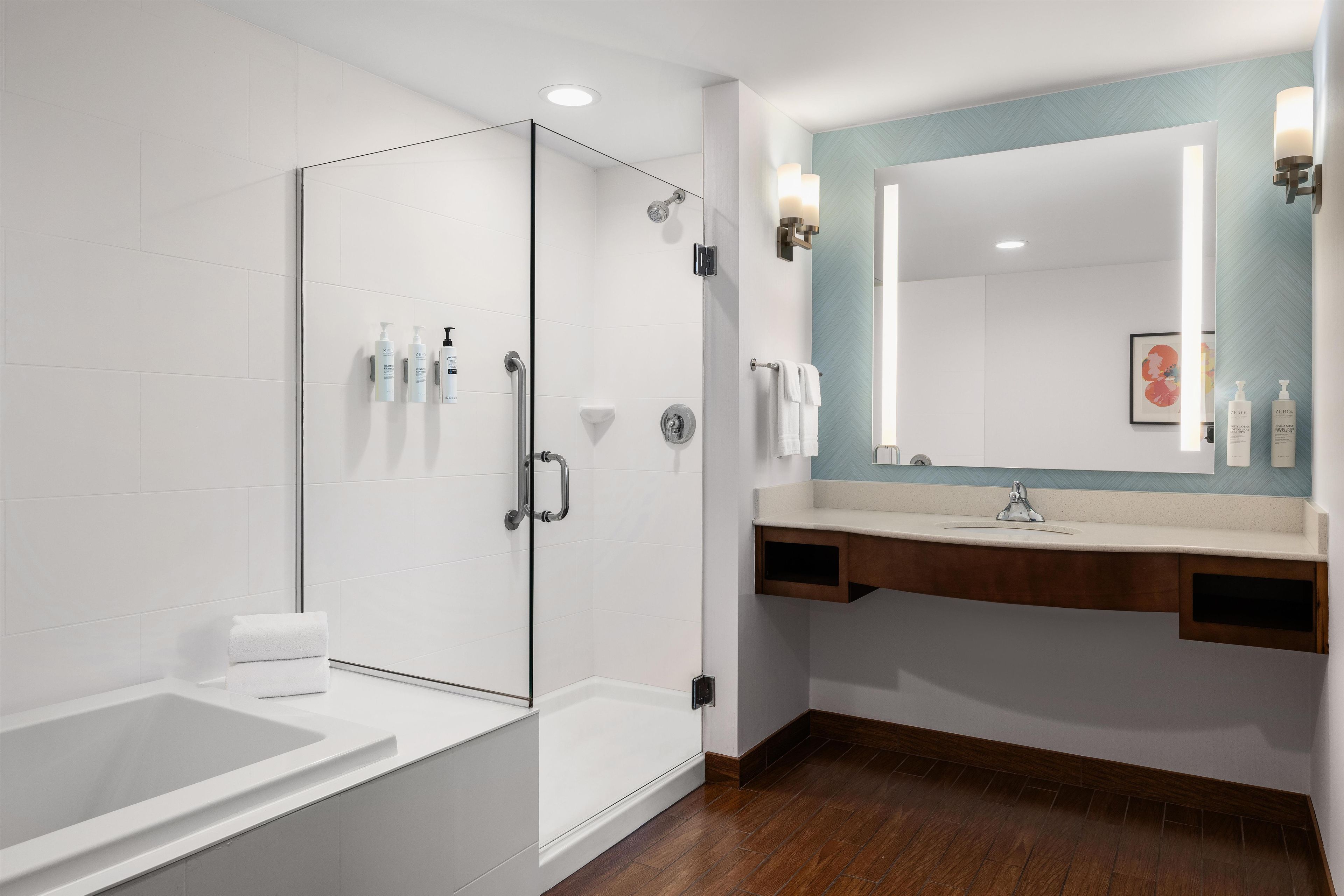 A modern bathroom with a glass-enclosed shower, a white bathtub, a wooden vanity with a mirror, and a white sink.