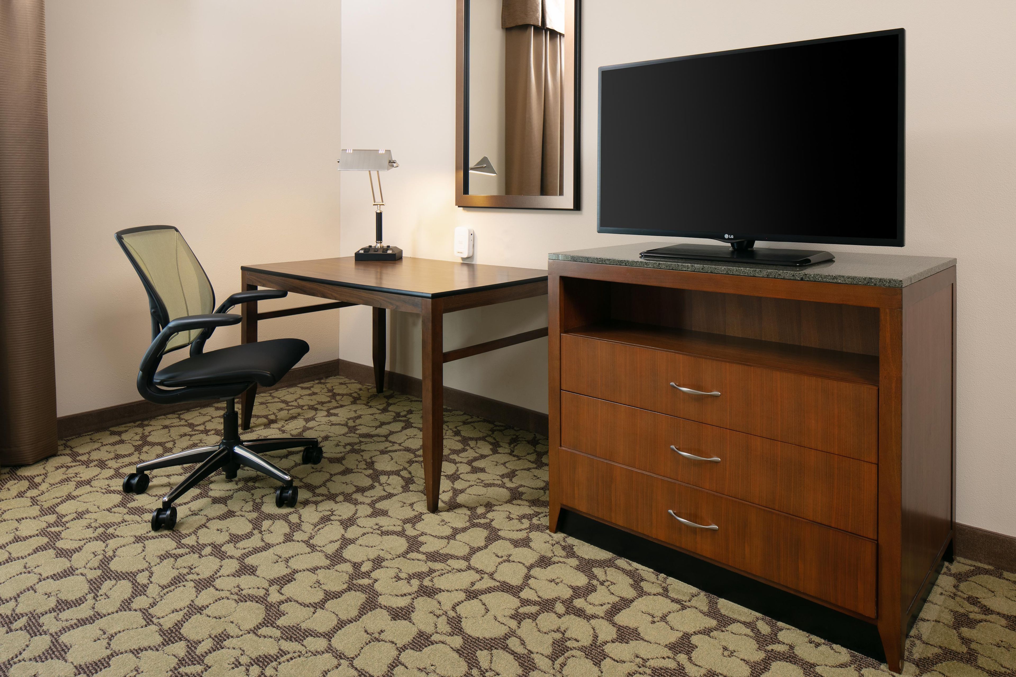 A hotel room with a desk, chair, TV, and wooden cabinet.