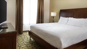 A hotel room with a large bed, a desk with a flat-screen TV, a lamp, and a window with curtains.