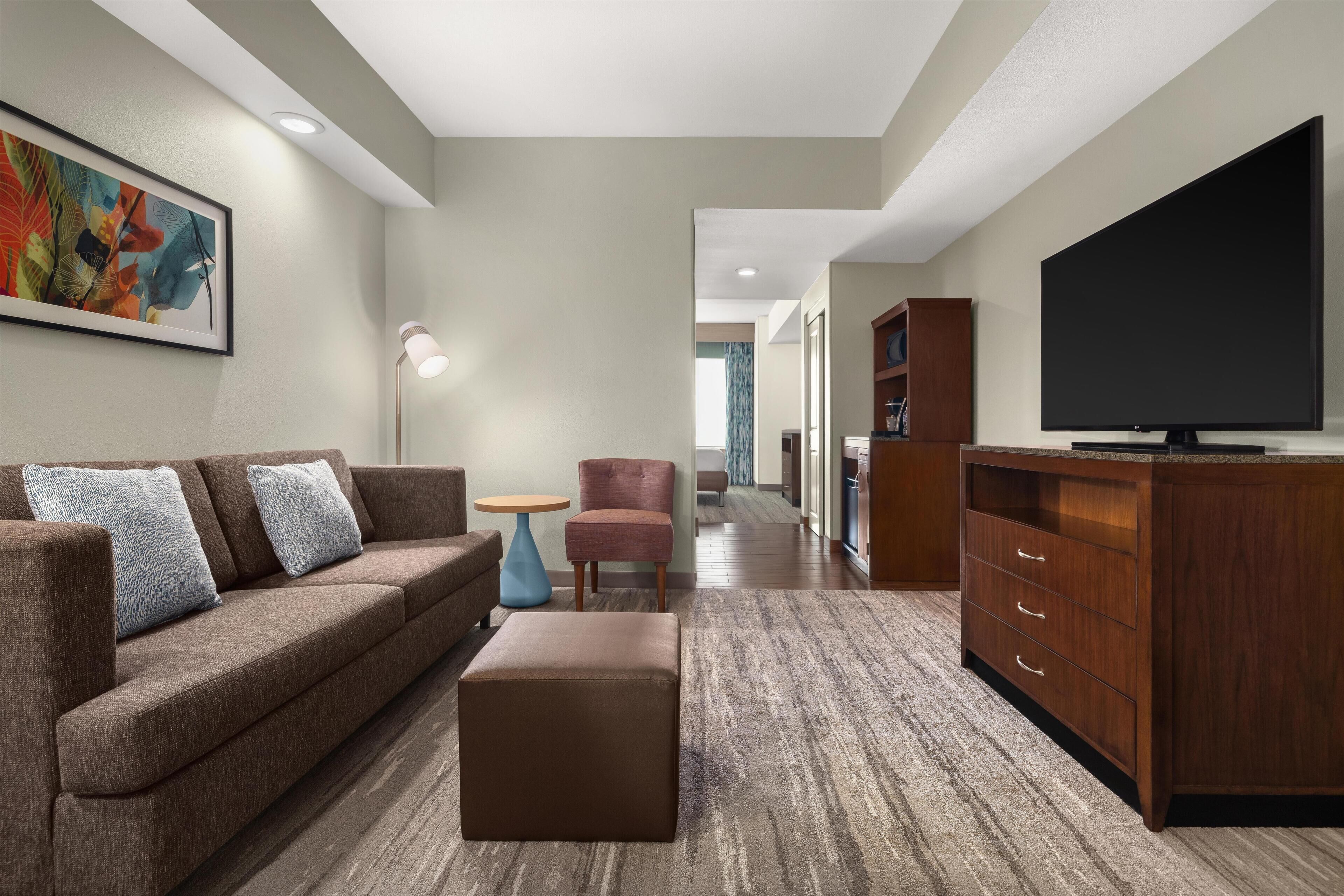 A modern living room with a sofa, ottoman, TV, and a small table.