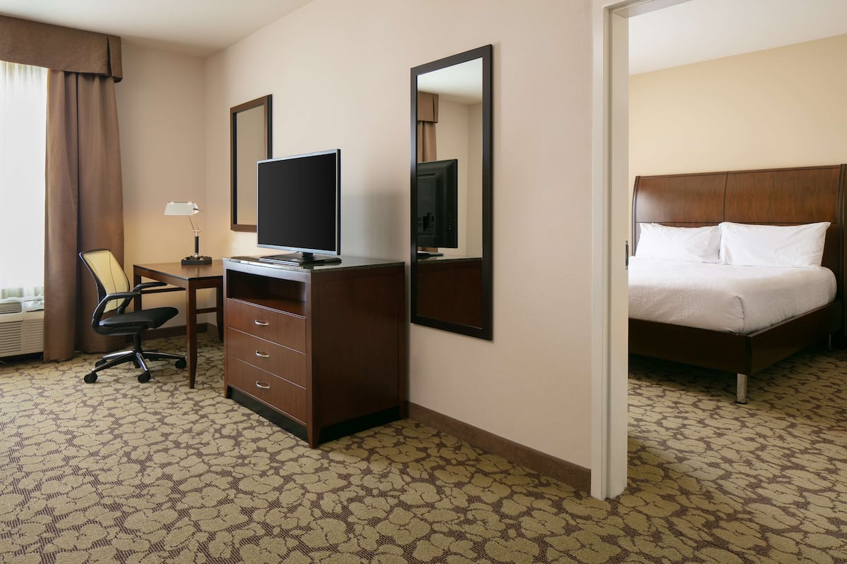 A hotel room with a bed, a desk with a chair, a television, and a dresser.