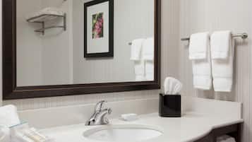 A hotel bathroom with a large mirror, a sink, a towel rack, and a framed picture on the wall.