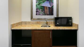 A kitchenette with a framed picture, a sink, a microwave, and a dishwasher.