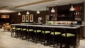 A bar area with a long counter, multiple bar stools, hanging pendant lights, and a well-stocked liquor shelf.