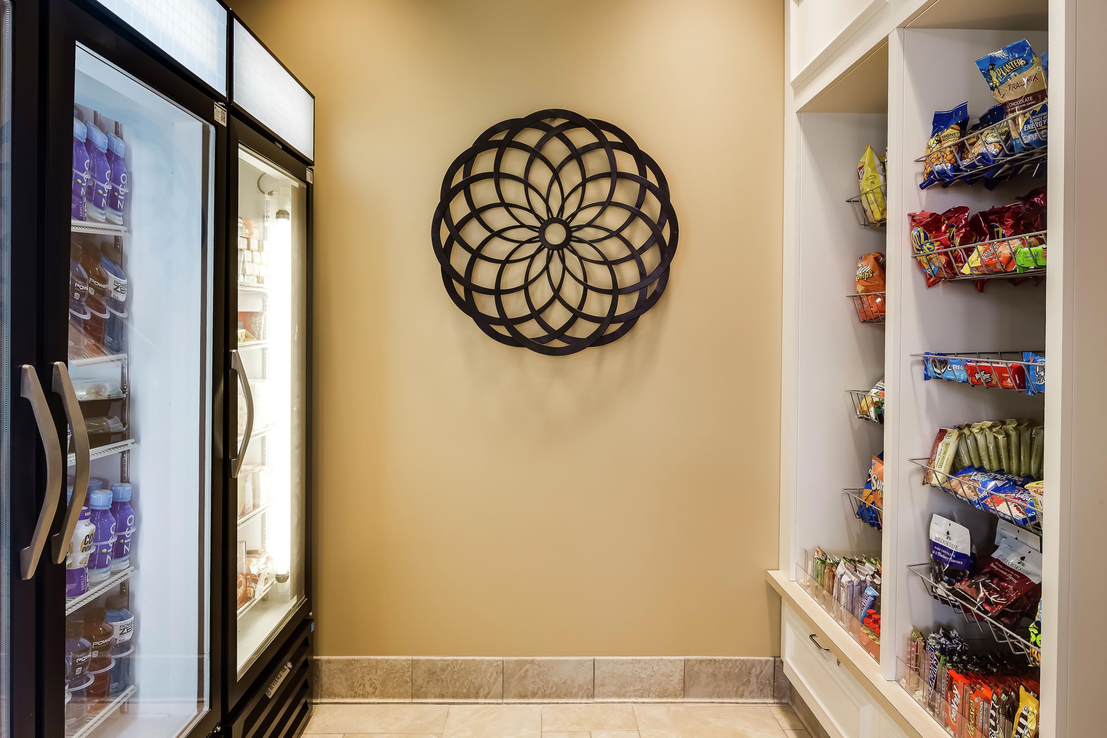 A hallway with a decorative wall piece, a refrigerated beverage display, and shelves stocked with snacks.
