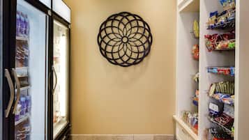 A hallway with a decorative wall piece, a refrigerated beverage display, and shelves stocked with snacks.