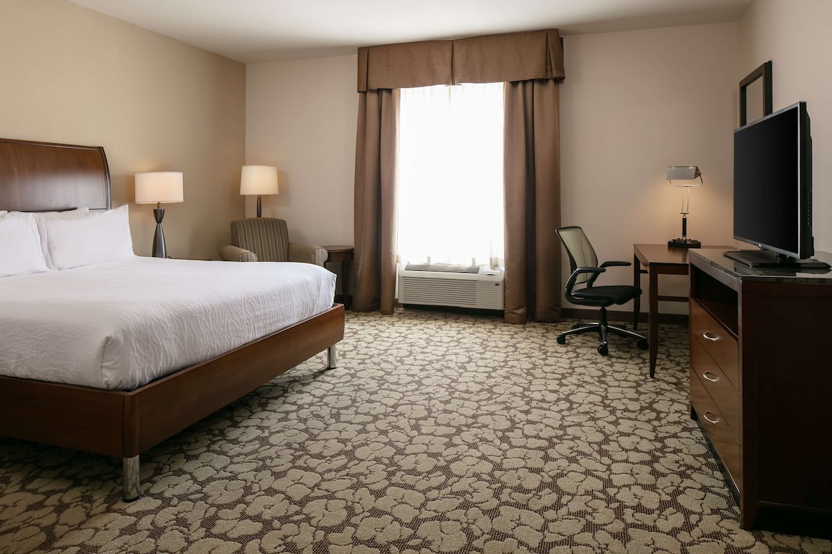 A hotel room with a bed, a desk, a chair, a television, and an air conditioning unit.