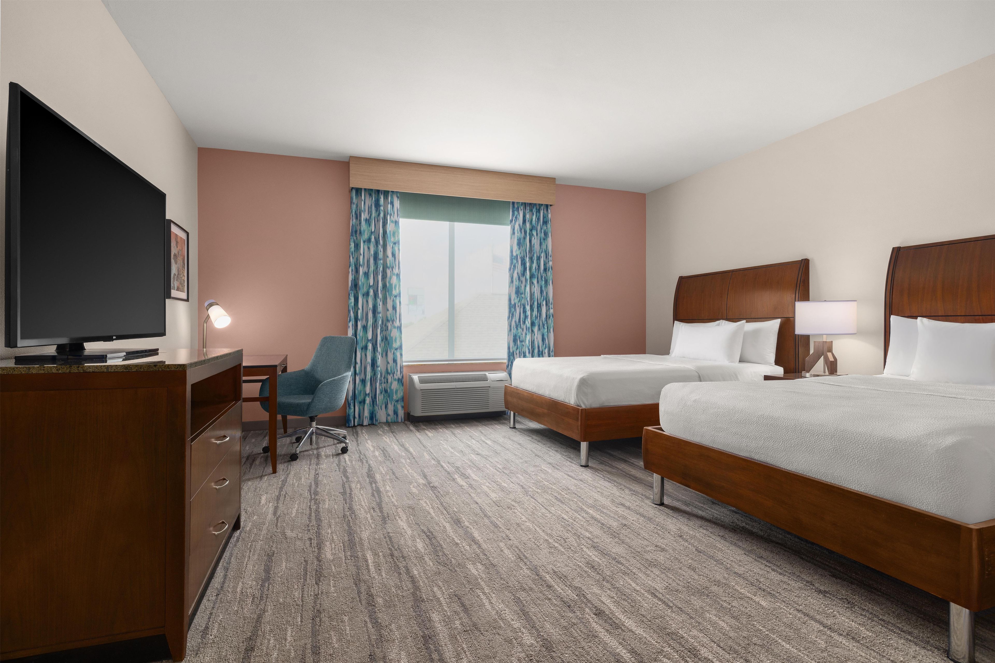 Een hotelkamer met een bed, bureau, stoel, televisie en een raam met gordijnen.