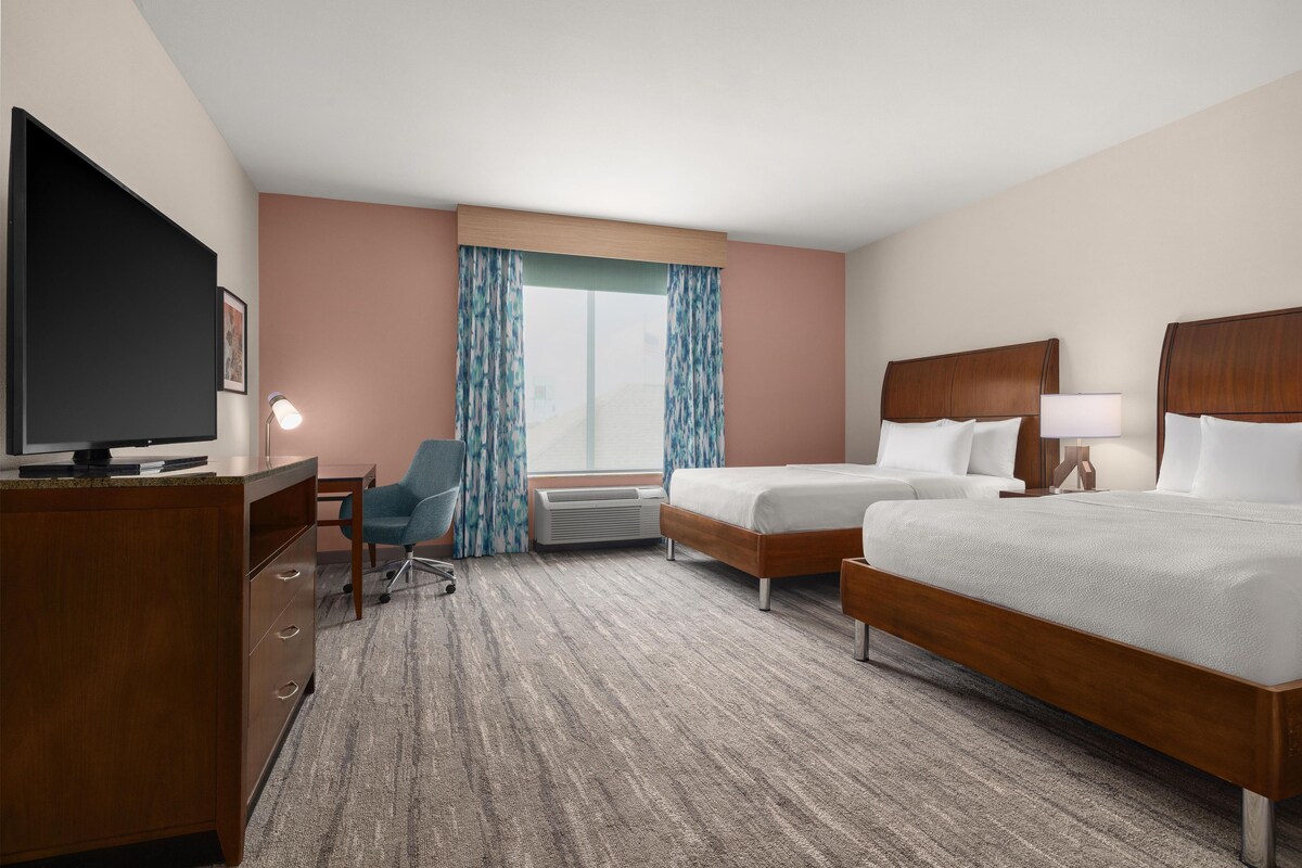 Een hotelkamer met een bed, bureau, stoel, televisie en een raam met gordijnen.