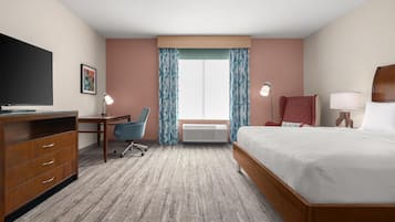 A hotel room with a bed, desk, chair, TV, and a large window with curtains.