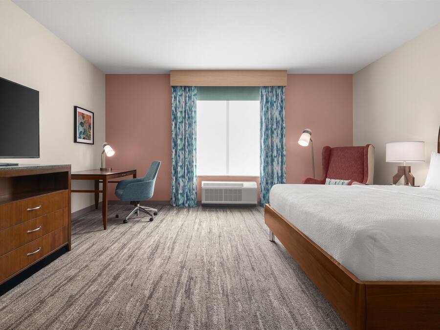 A hotel room with a bed, desk, chair, TV, and a large window with curtains.