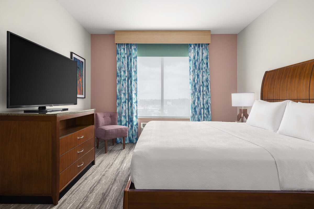 Een hotelkamer met een bed, een televisie, een bureau, een stoel en een raam met gordijnen.