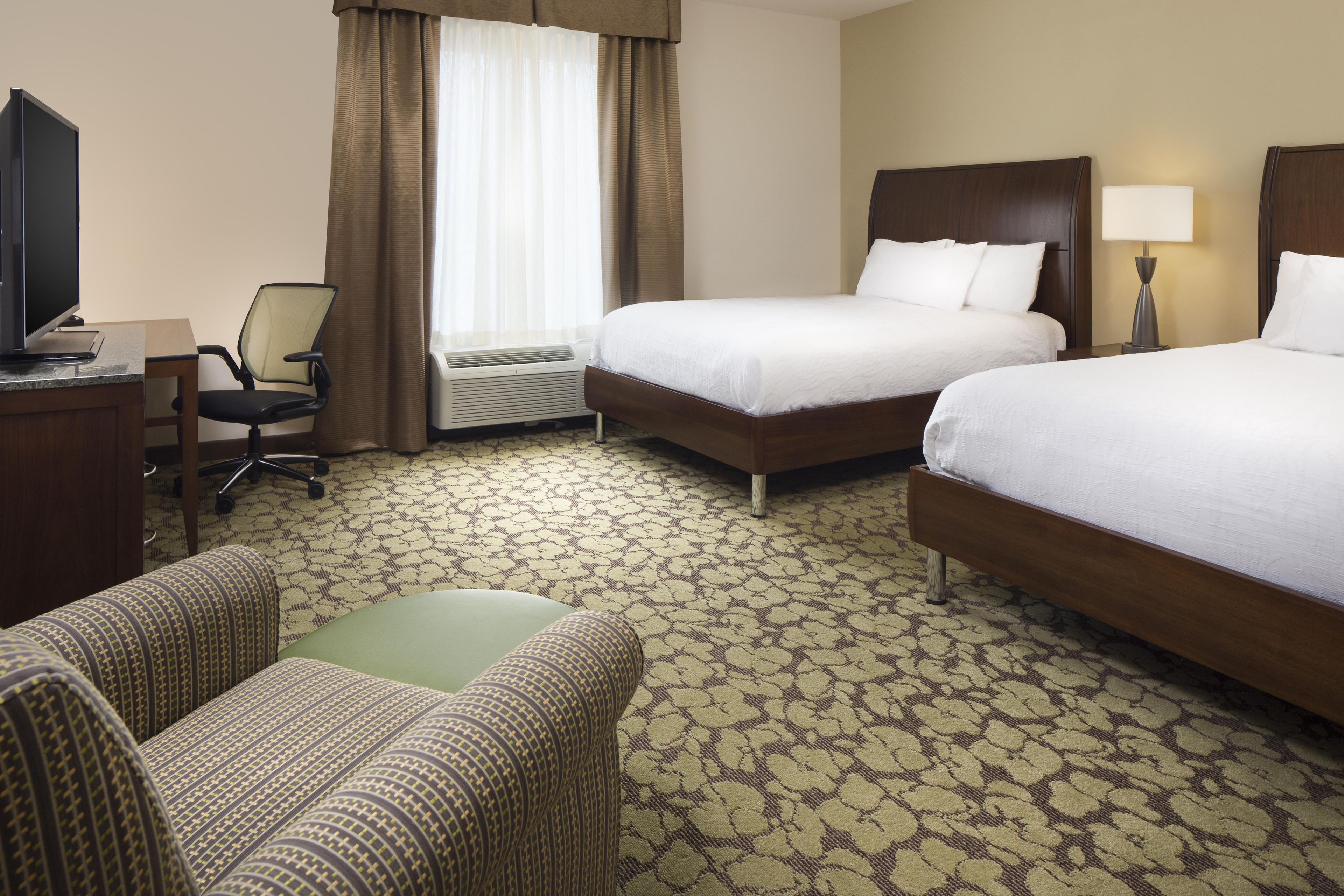 A hotel room with two beds, a desk with a computer, a chair, and a lamp.