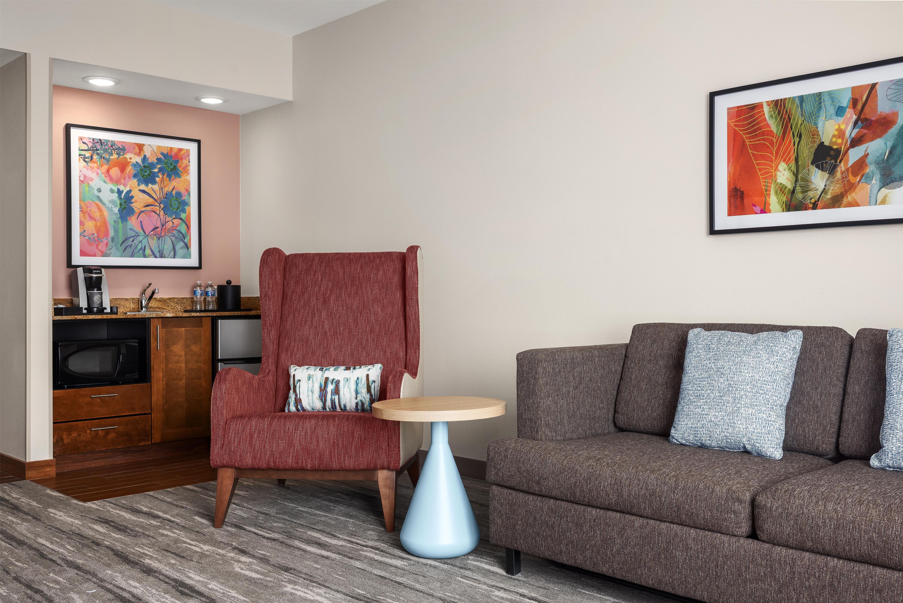 Un salón moderno con un sillón rojo, un sofá marrón y dos mesitas.