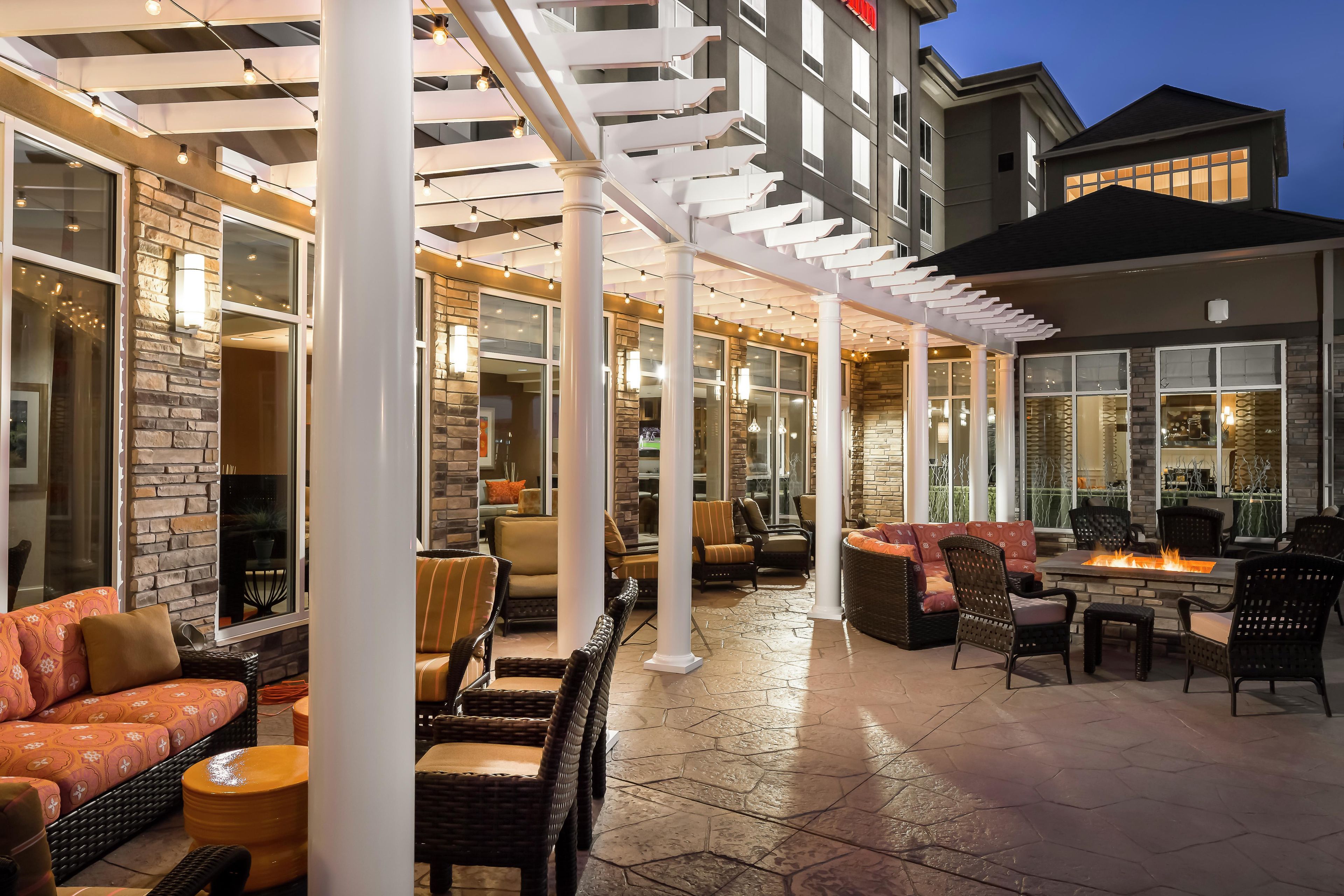 An outdoor patio area with seating arrangements, a fire feature, and a view of the building's interior.