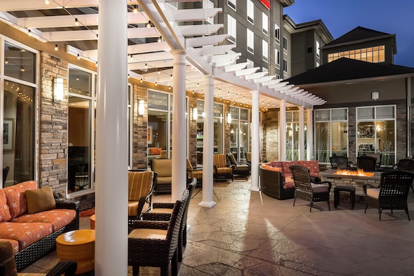 An outdoor patio area with seating arrangements, a fire feature, and a view of the building's interior.