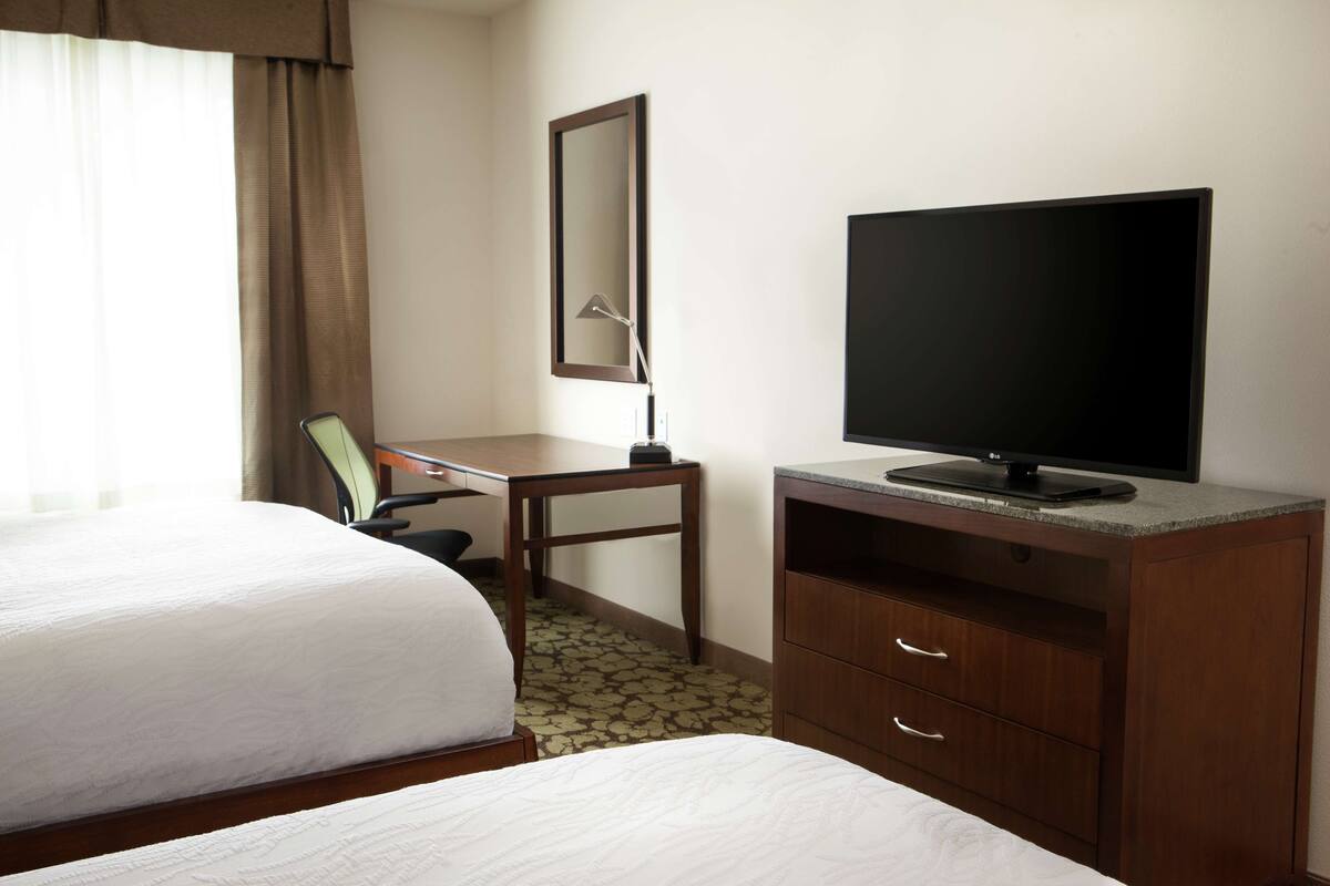 A hotel room with two beds, a desk, a television, and a mirror.