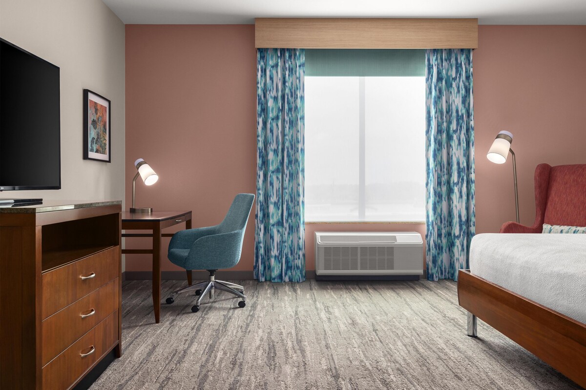 Hotelkamer met een bed, bureau, stoel, televisie, airconditioning en gordijnen.