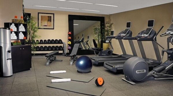 Een fitnessruimte met loopbanden, elliptische trainers, een hometrainer, losse gewichten en een waterdispenser.