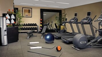 Un gimnasio con cintas de correr, elípticas, una bicicleta estática, pesas libres y un dispensador de agua.