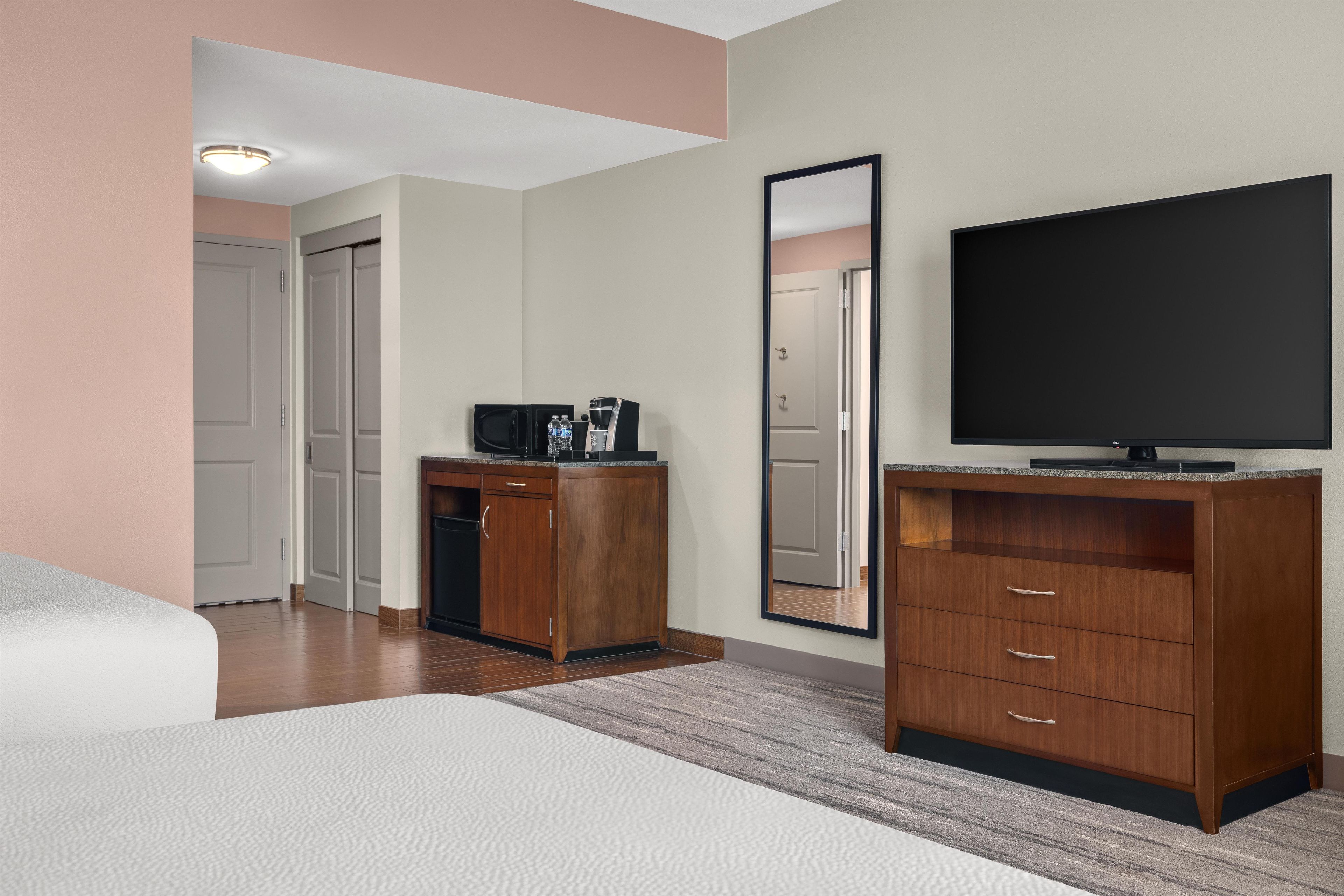 A hotel room with a bed, a desk with a coffee maker, a television, and a mirror.