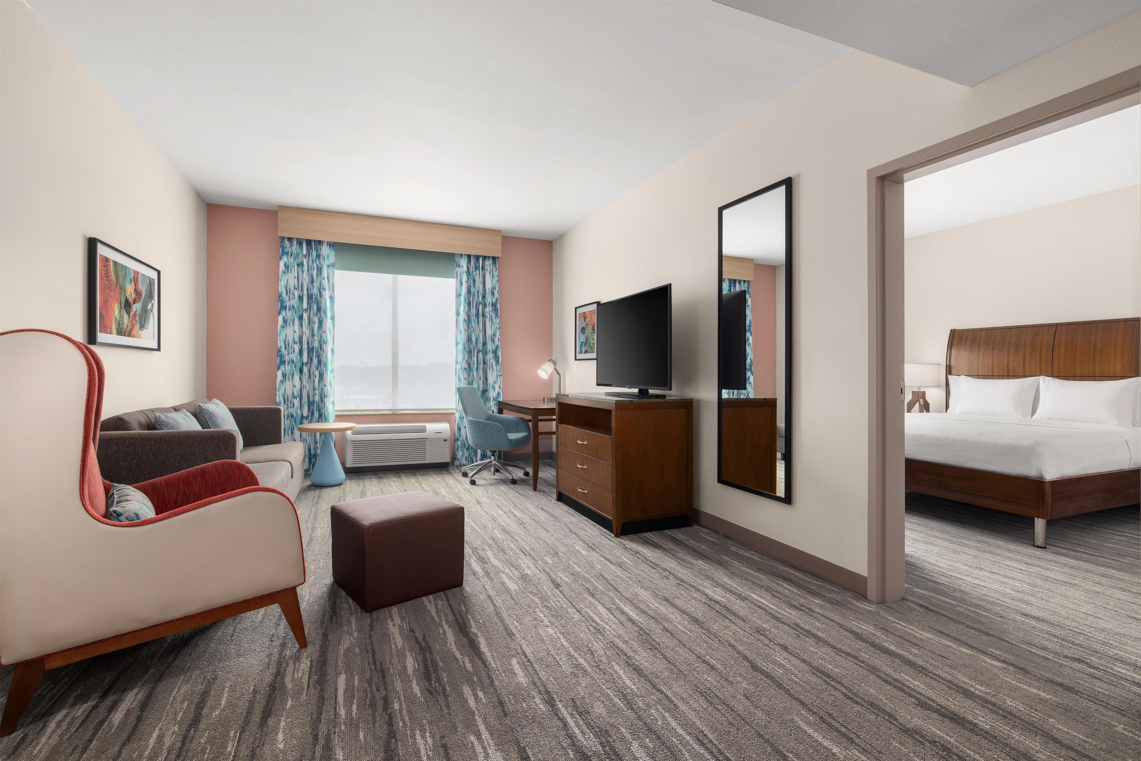 A hotel room with a bed, a desk with a computer, a chair, a TV, and a window with curtains.