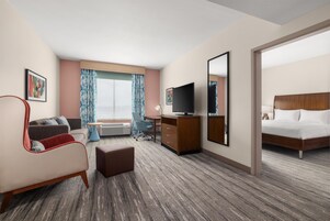 Habitación de hotel con cama, escritorio con computadora, silla, televisor y ventana con cortinas.