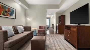 A modern living room with a sofa, ottoman, TV, and a small table.