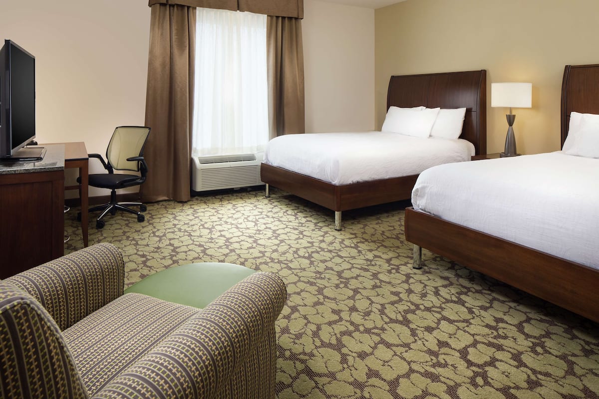 A hotel room with two beds, a desk with a computer, a chair, and an air conditioning unit.