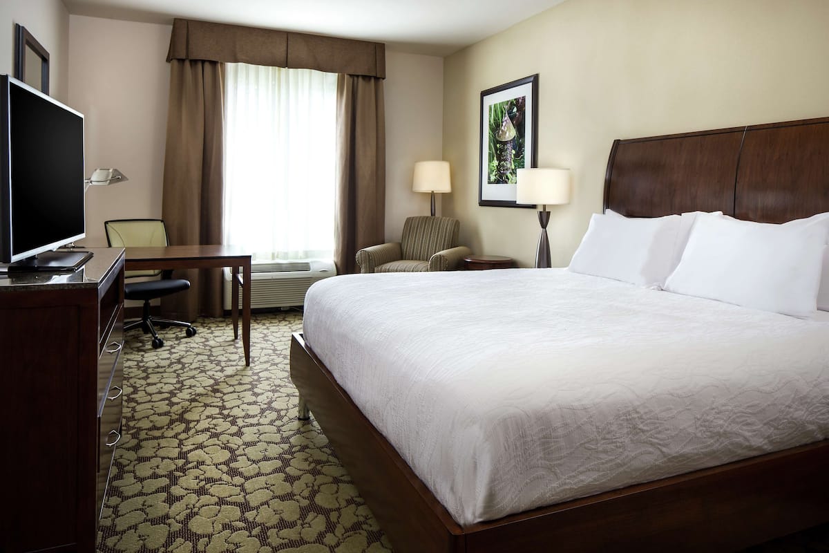 A hotel room with a large bed, a desk with a TV, a chair, and a window with curtains.