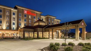 A multi-story hotel with a prominent 'Hilton Garden Inn' sign, a covered entrance, and a landscaped area with a small tree.