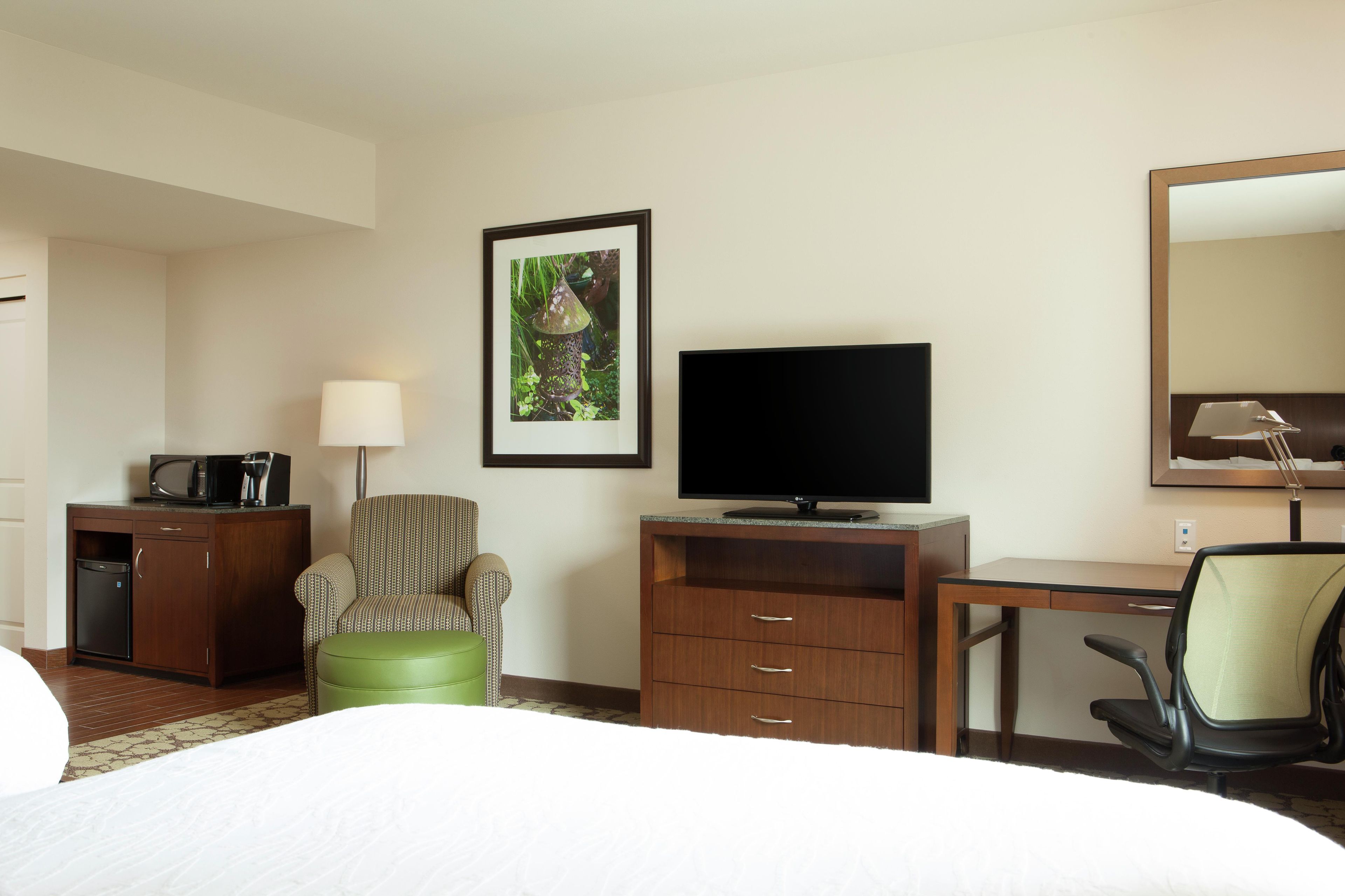 Habitación de hotel con cama, escritorio con televisor de pantalla plana, una silla, un mueble pequeño y un cuadro en la pared.