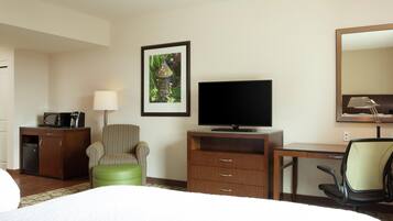 Habitación de hotel con cama, escritorio con televisor de pantalla plana, una silla, un mueble pequeño y un cuadro en la pared.