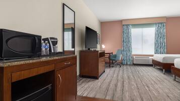 Hotelkamer met kitchenette, flatscreen-tv, bureau met stoel, bed en groot raam met gordijnen.
