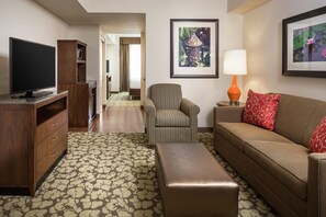 Une chambre d’hôtel équipée d’un téléviseur à écran plat, d’un canapé, d’un tapis à motifs, d’un tableau encadré et d’une lampe.
