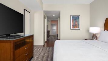 Habitación de hotel con cama, televisor en una cómoda de madera, un cuadro en la pared y un pasillo que conduce a un baño.