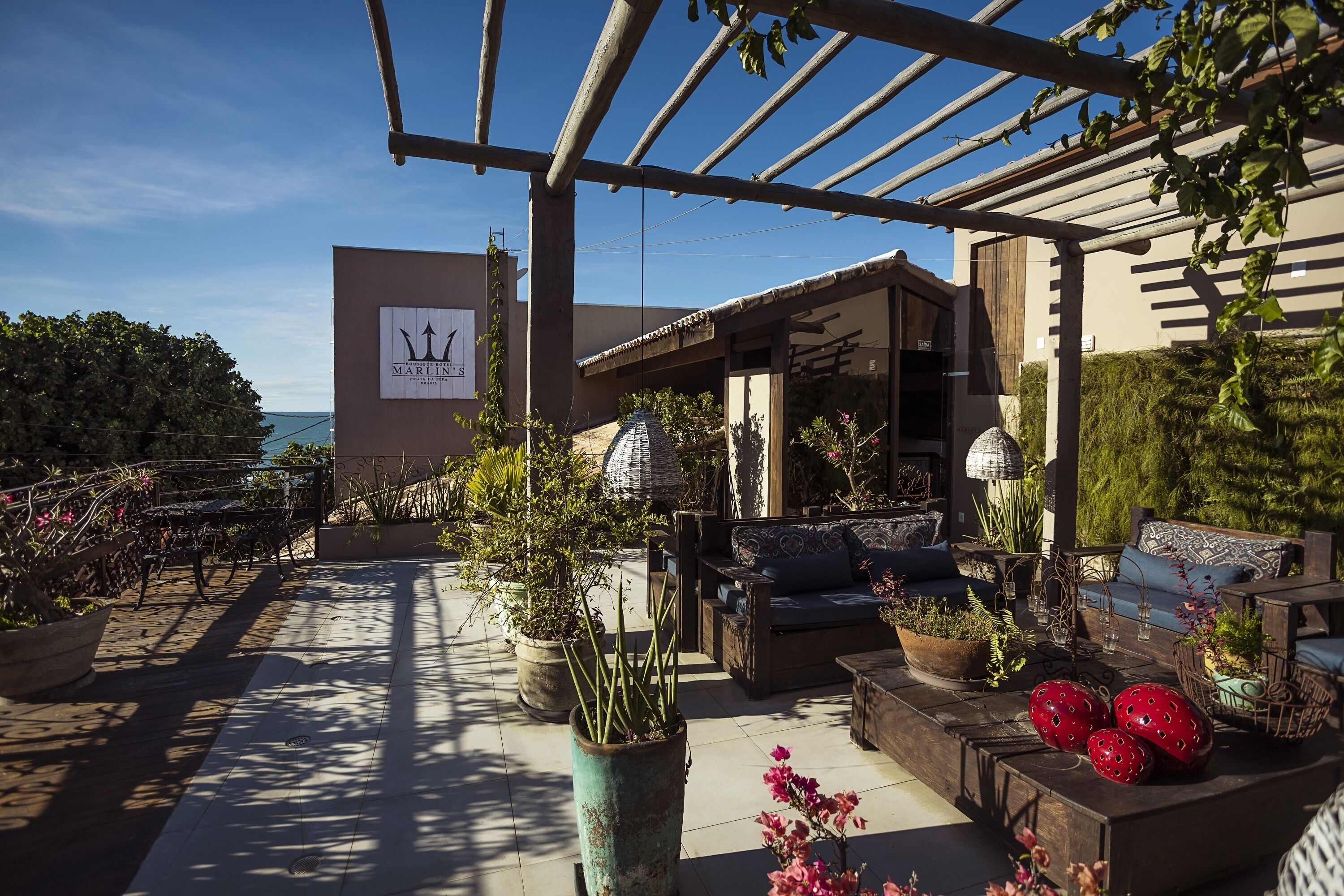 Un área de patio al aire libre con mobiliario, plantas en macetas y una pérgola.