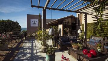 Un área de patio al aire libre con mobiliario, plantas en macetas y una pérgola.