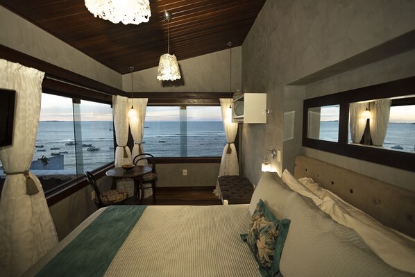Une chambre avec un grand lit, une vue sur la mer, une petite table avec une chaise et un téléviseur.