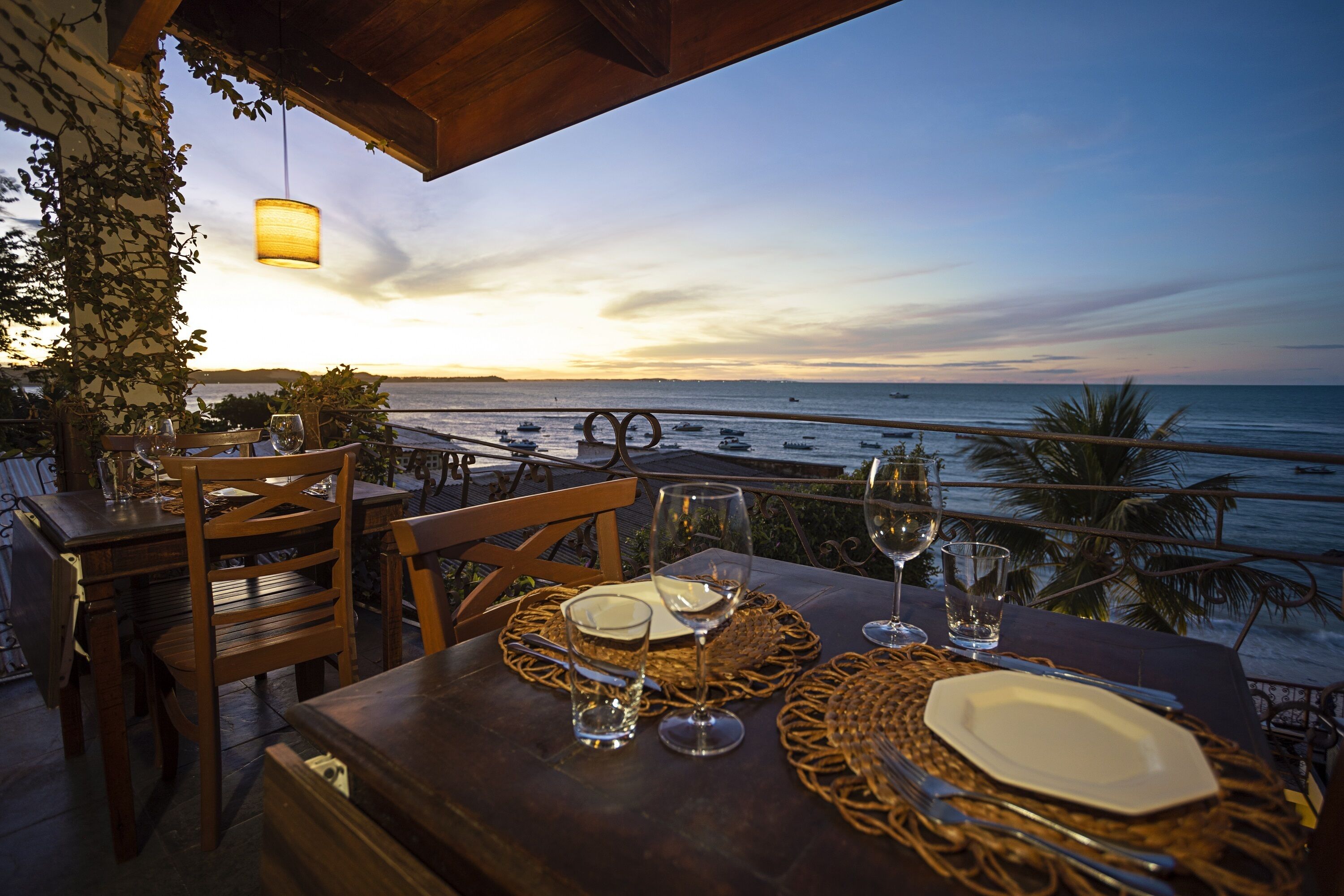A table set for dining with a view of the ocean and boats at sunset.