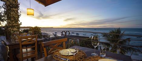 A table set for dining with a view of the ocean and boats at sunset.