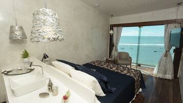 A bedroom with a bed, a bedside table with a sink, a chair, and a view of the ocean.