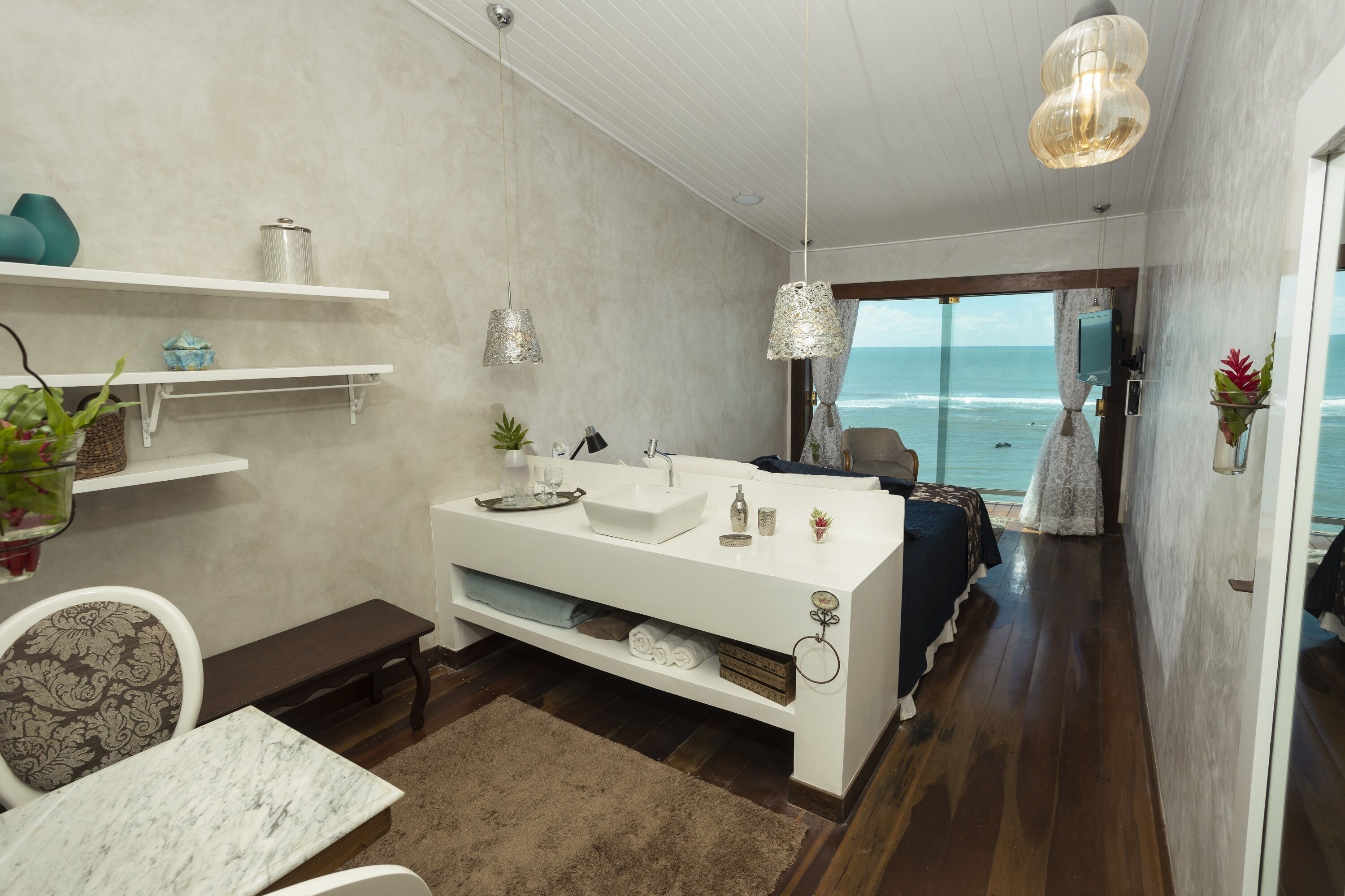 A modern bathroom with a white vanity, a large mirror, and a view of the ocean.