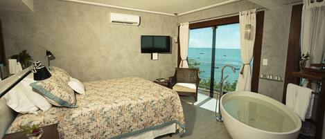 A bedroom with a large bed, a bathtub, a television, and a view of the sea.
