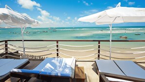 Eine Strandlounge mit weißen Sonnenschirmen und Holzliegen mit Blick auf den Ozean.