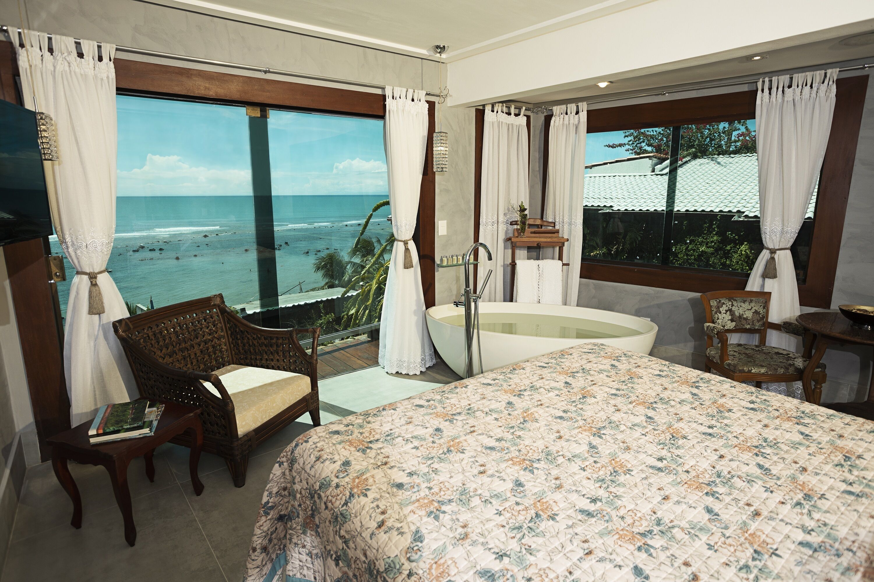 Een slaapkamer met een groot bed, een badkuip, uitzicht op de oceaan en een balkon met een stoel.